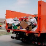 Orange dump truck loaded with household debris and clutter in a driveway for Junk removal services kent wa